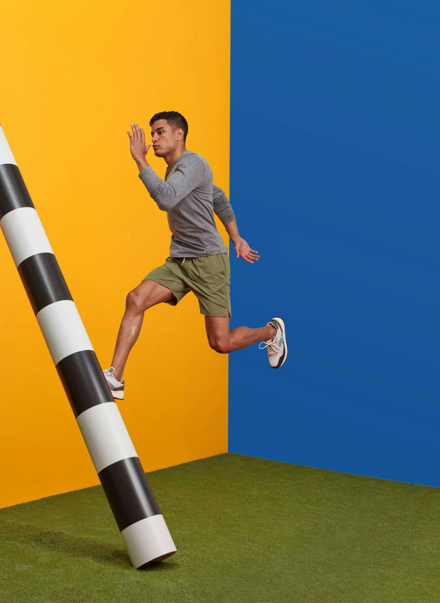 Man leaping in front of a blue and yellow background near a black and white striped pole