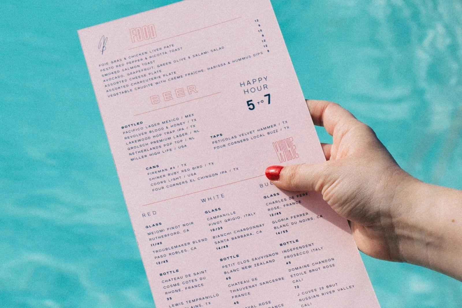 Hand holding a food and drinks menu by the pool