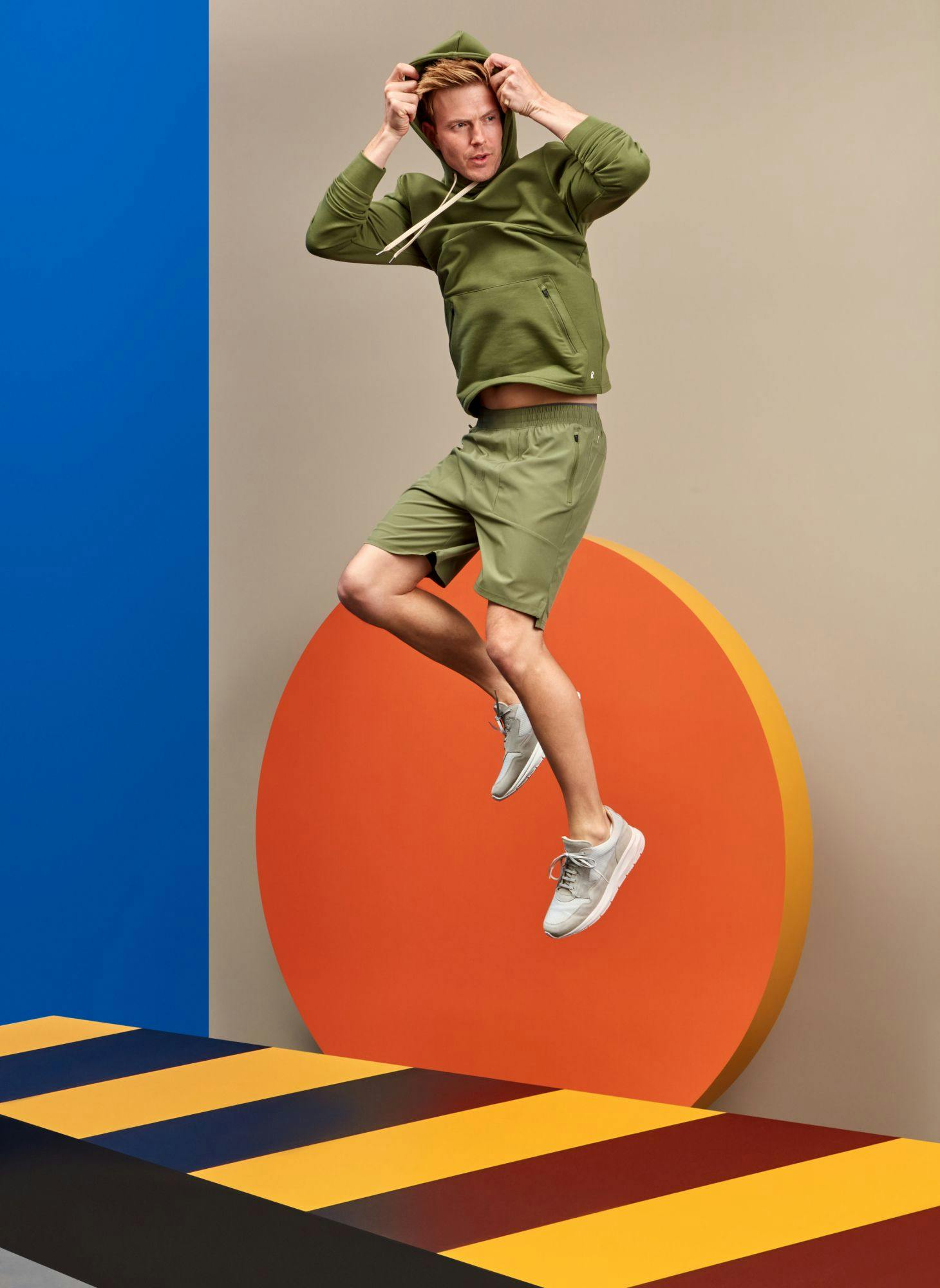 Man in green activewear jumping with an orange and blue background
